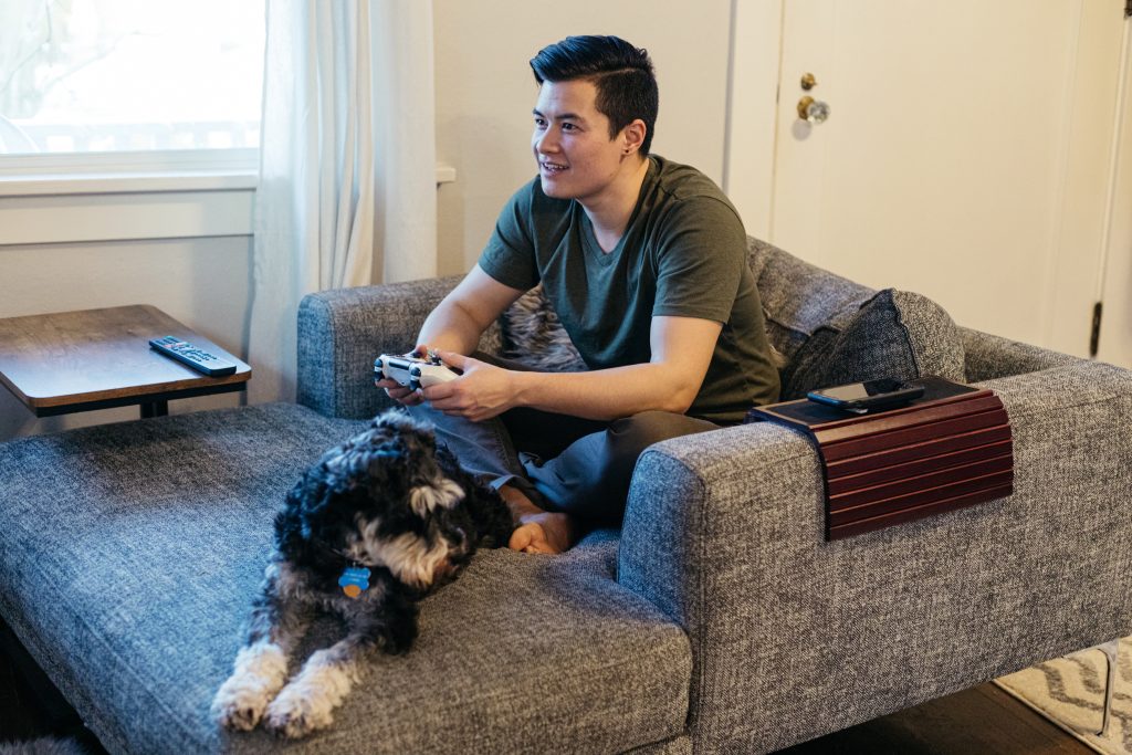 homem jogando video-game sentado no sofá ao lado de seu cachorro representando os hábitos de consumo dos gamers em relação ao seu pet