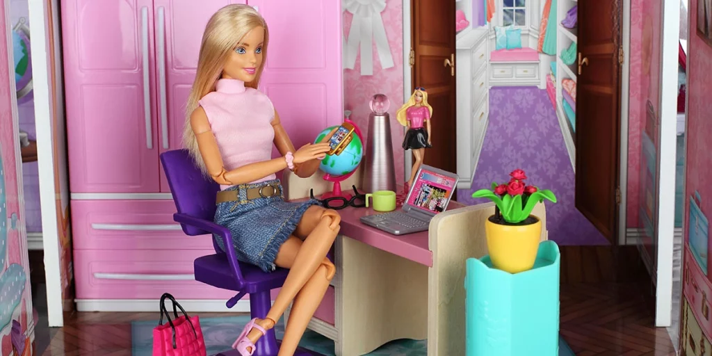 Barbie sentada na casa da Barbie em escritório de brinquedo com objetos e decoração em tons de rosa