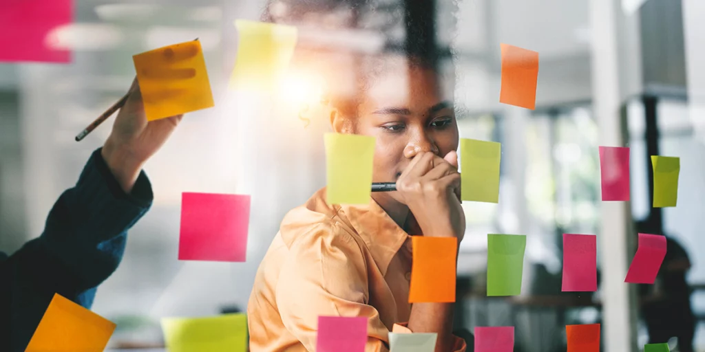 profissional de criação fazendo anotações em post-it grudado em parede de vidro